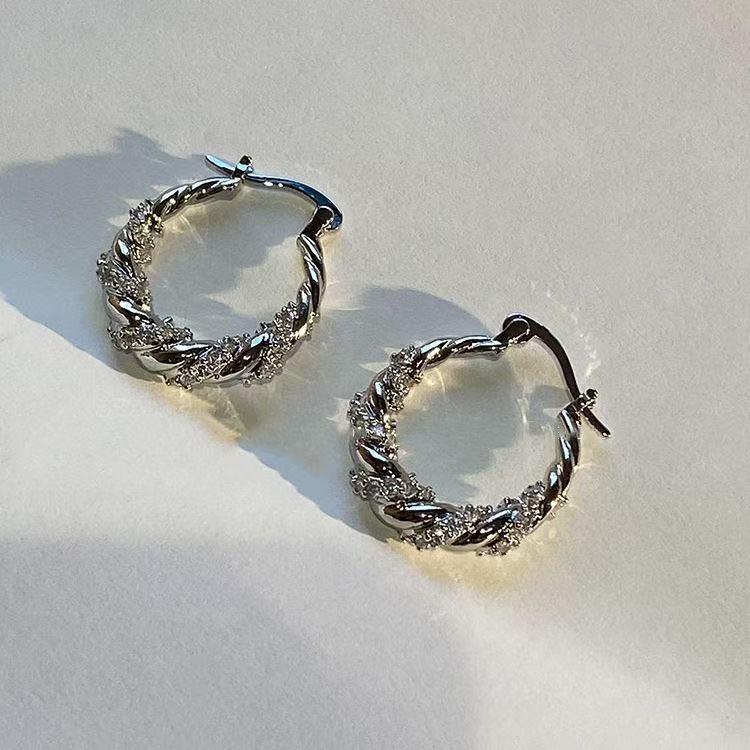Silver twisted hoop earrings with alternating crystal and polished sections on white background, casting soft shadows