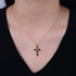 A woman wearing gold sapphire cross necklace with diamond center against black top on pale skin
