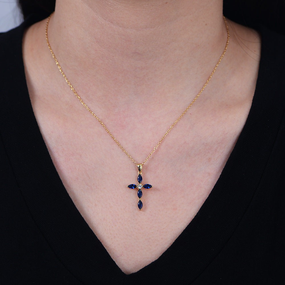 A woman wearing gold sapphire cross necklace with diamond center against black top on pale skin