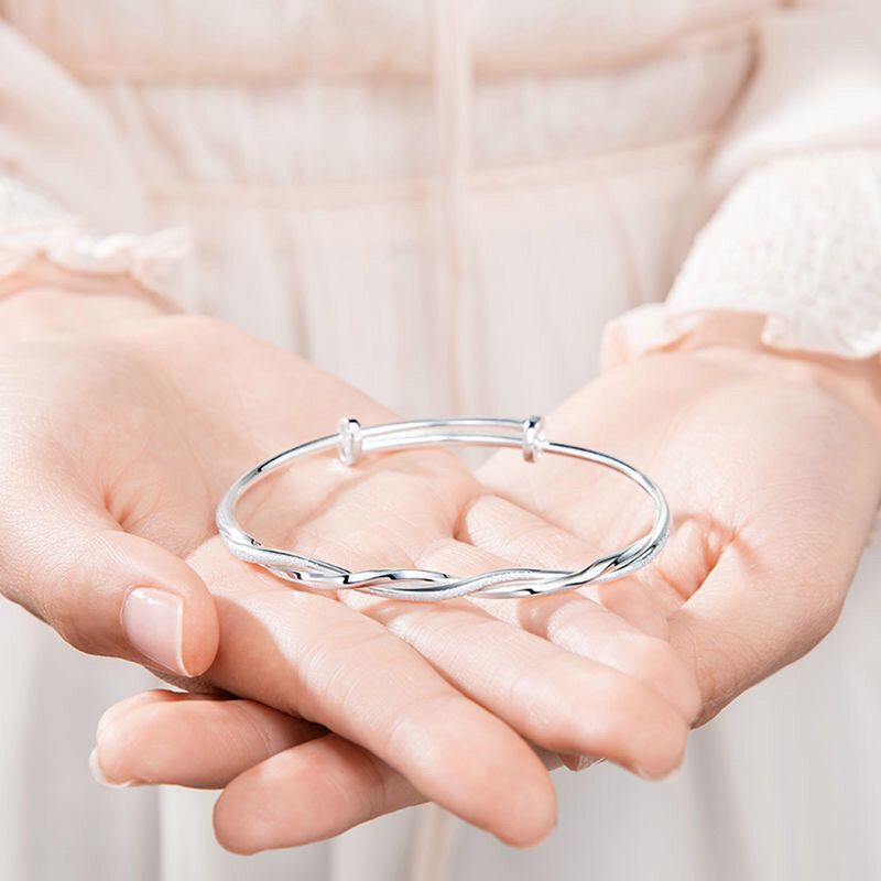 A woman holding a silver twisted bangle bracelet in open palms, wearing white textured clothing