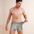 Model wearing light gray boxer briefs, showcasing fit and fabric against neutral background