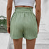 Back view of sage green pleated shorts showing paperbag waist detail and textured fabric, styled with white crop top