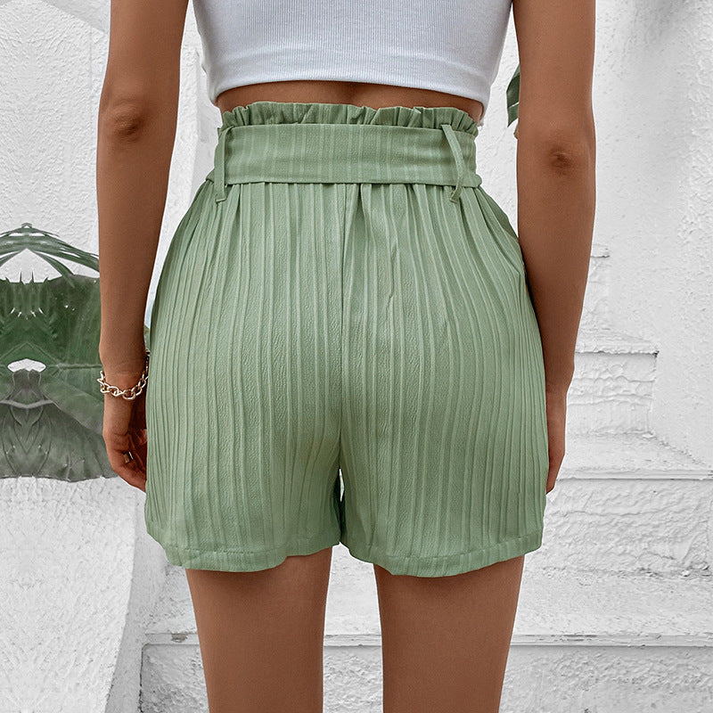 Back view of sage green pleated shorts showing paperbag waist detail and textured fabric, styled with white crop top