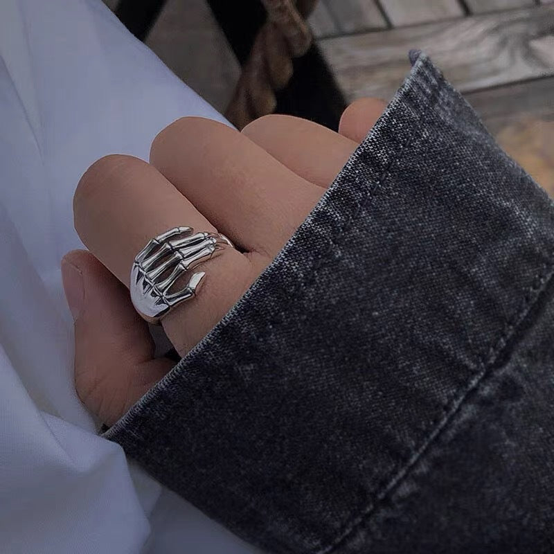 Silver skeleton hand ring on a hand partially covered by a dark denim sleeve, creating a gothic aesthetic