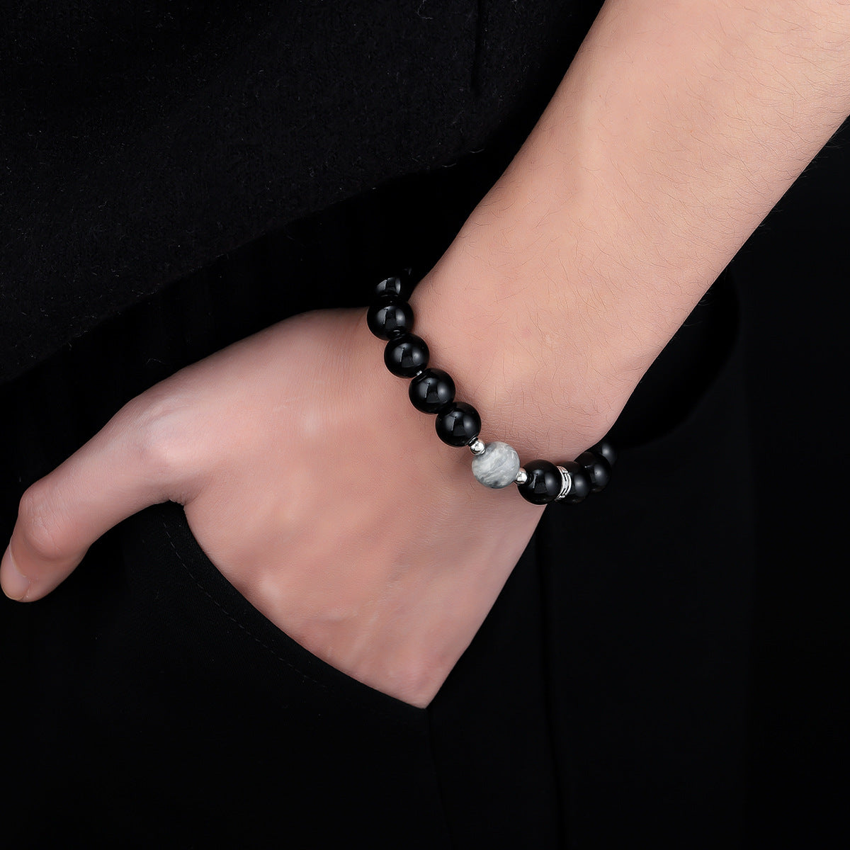 Black beaded bracelet with a gray marbled bead, worn on a wrist with a hand resting inside a pocket.