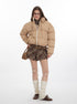 Full-body shot of a woman wearing a beige puffer jacket, plaid skirt, knee-high knit leg warmers, and brown loafers