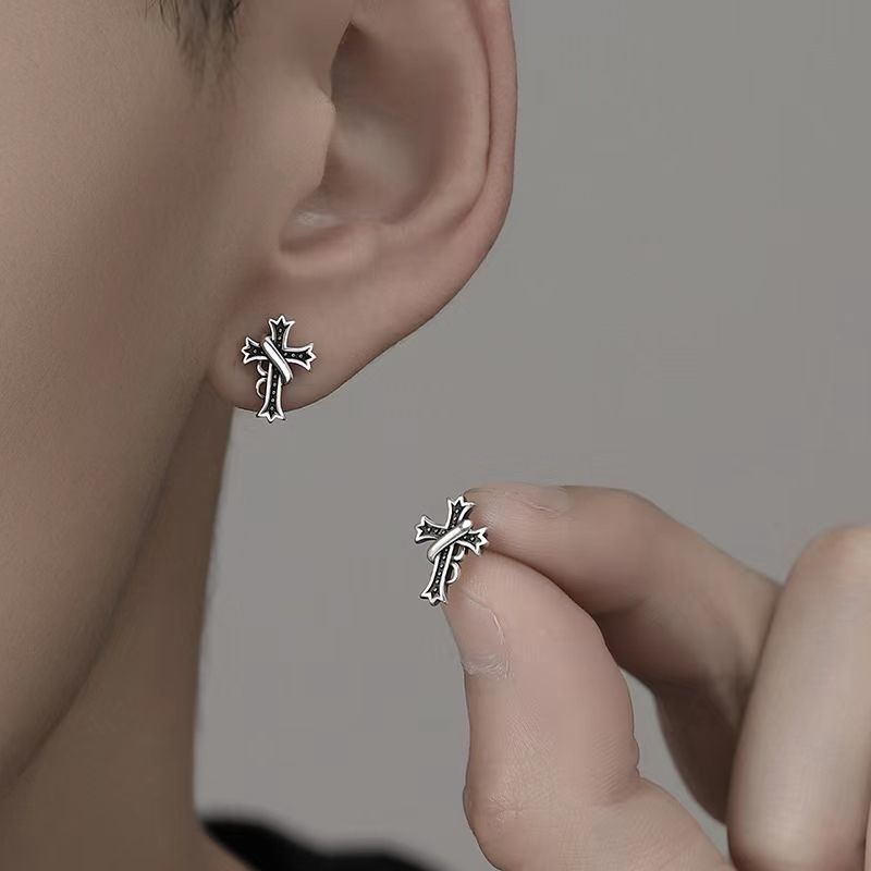 Cross stud earring worn on ear with another being held, showing ornate vintage style
