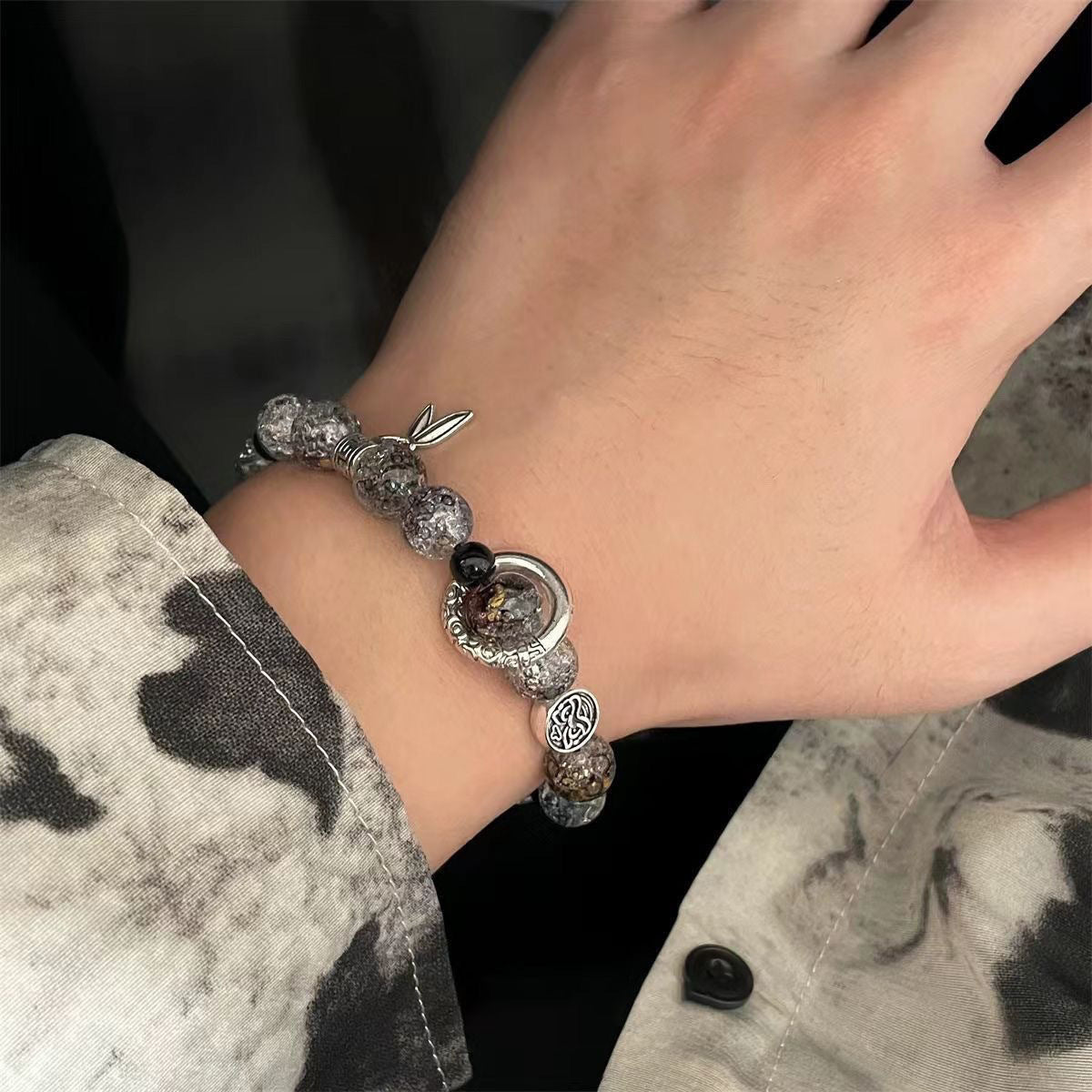 Bracelet styled on wrist showing crystal beads and silver charms against tie-dye fabric