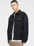 A model is showing the quilted lining of a black checkered jacket over white graphic tee and tan pants against white backdrop