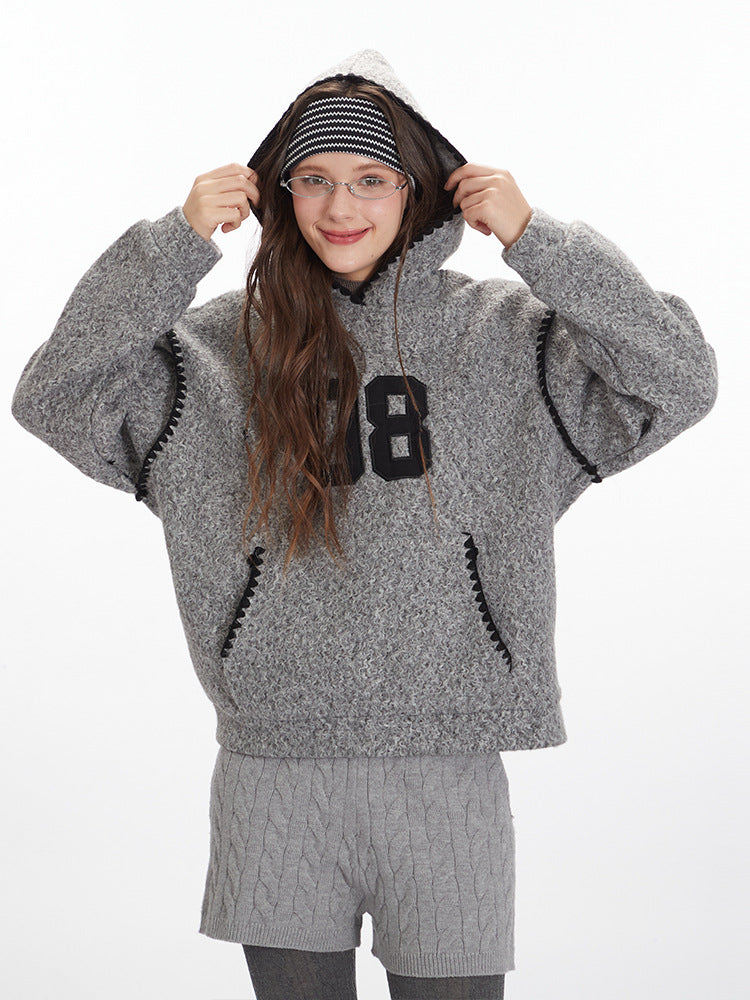 Close-up of grey textured hoodie highlighting '08' graphic appliqué, black whipstitch trim, and hood construction. Shown with grey cable knit shorts