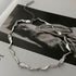 Close-up of a silver abstract chain necklace displayed on a black-and-white fashion magazine