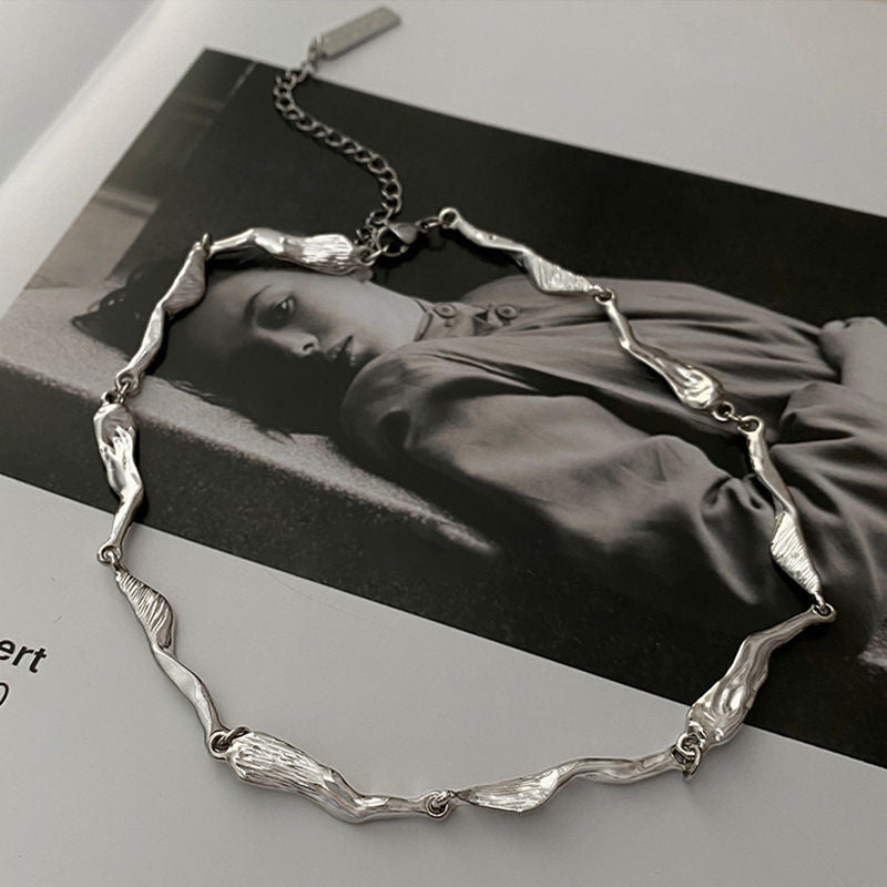 Close-up of a silver abstract chain necklace displayed on a black-and-white fashion magazine