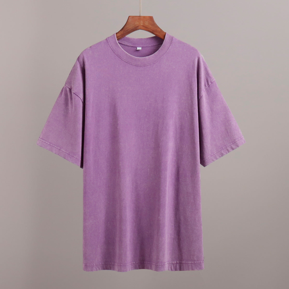 Purple t-shirt on a wooden hanger against a gray background