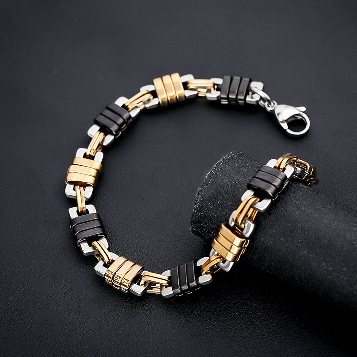  A detailed shot of the black and gold stainless steel bracelet on a black textured surface, showcasing the intricate link pattern and secure clasp.