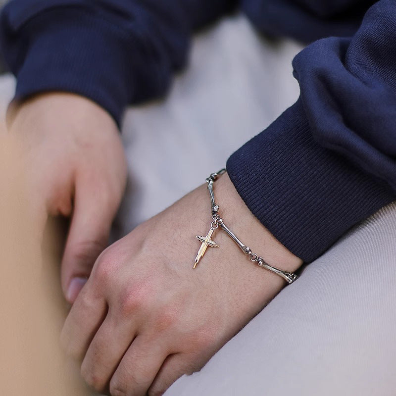 A silver bone-link bracelet with a gold cross charm on a person's wrist, styled with a navy sweater.