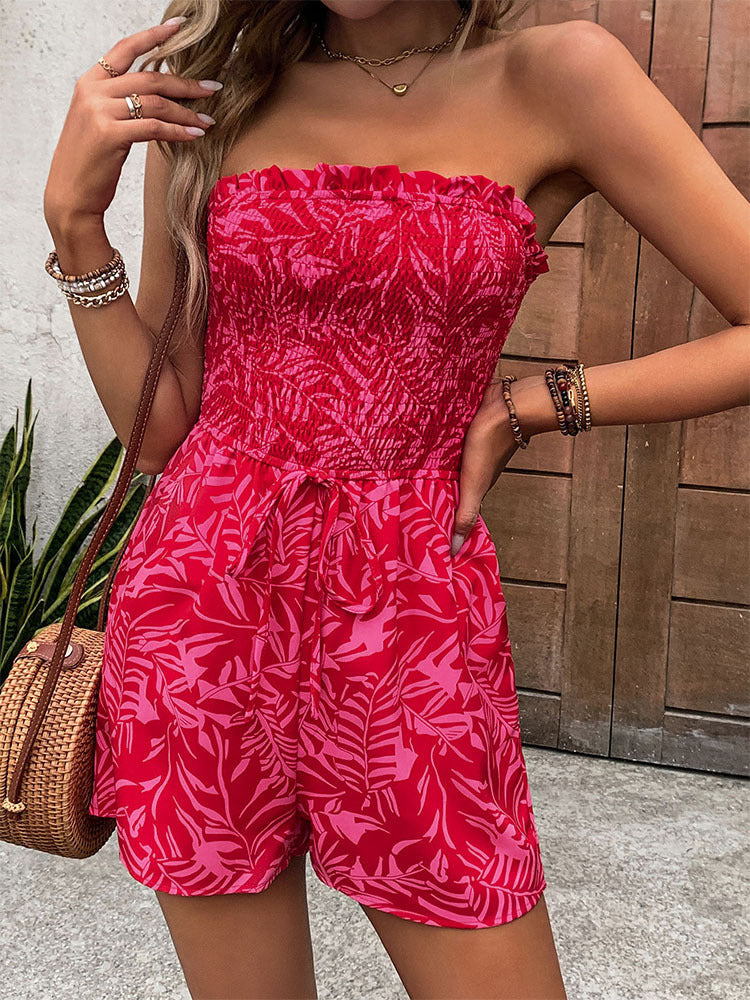 Close-up of a woman in a red off-shoulder romper with a ruched top and tropical print, posing with hand on hip.