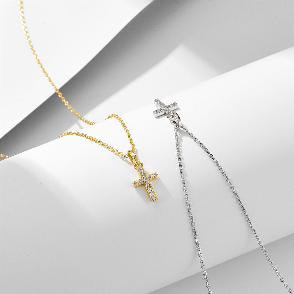 Gold and silver cross pendant necklaces displayed side by side on white geometric surface, both featuring diamond-set crosses