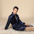 Man in navy silk robe sitting on white furry carpet, posing with robe partially open showing chest