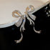Ornate silver bow earrings with crystal pavé detail displayed on white porcelain, showing dramatic sparkle effect