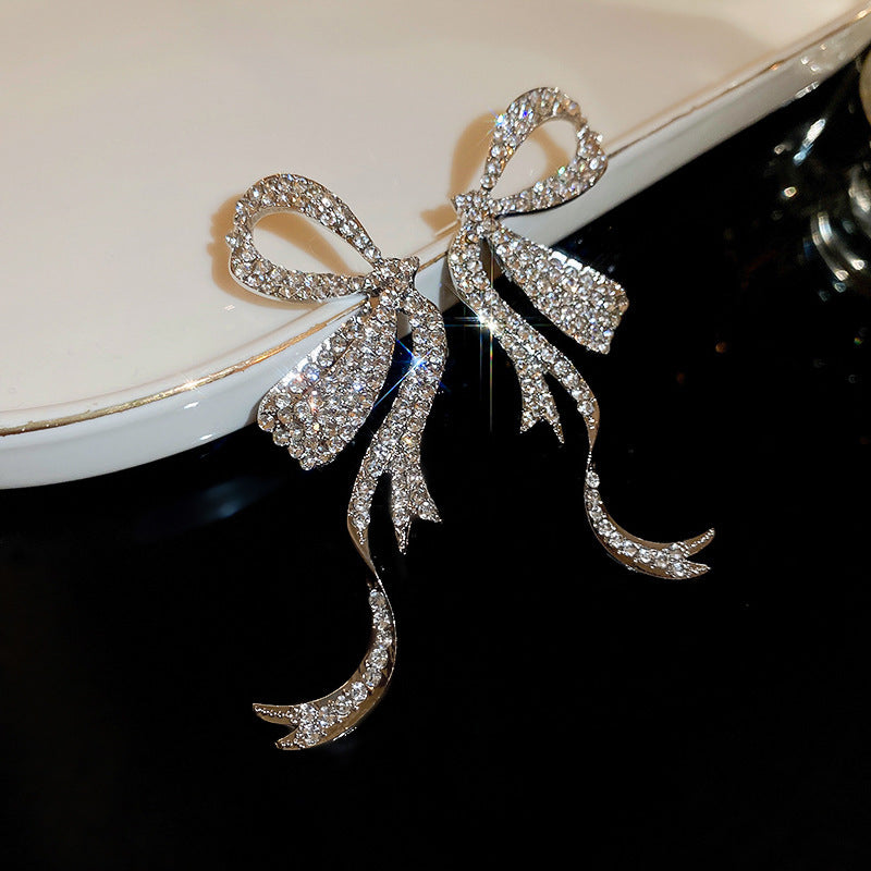 Ornate silver bow earrings with crystal pavé detail displayed on white porcelain, showing dramatic sparkle effect