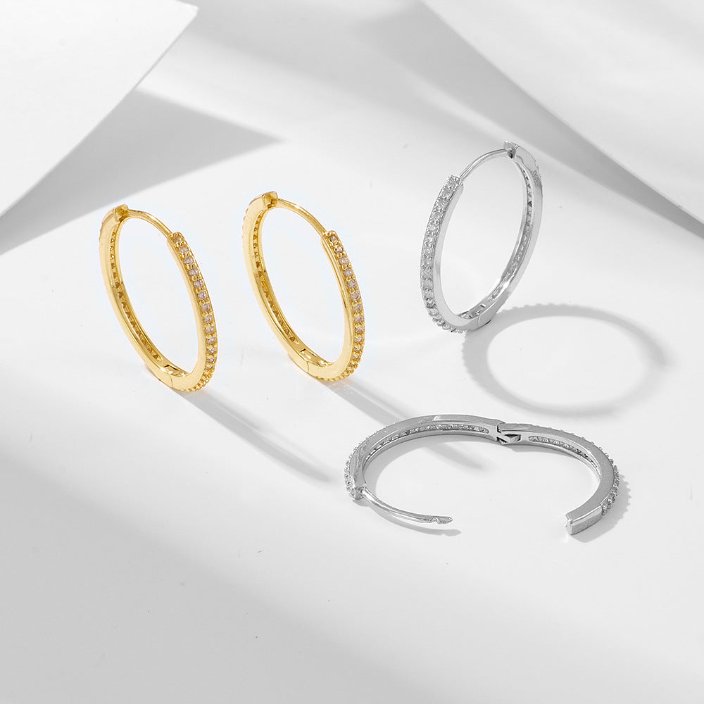 Diamond hoop earrings in gold and silver displayed on white surface. Two gold hoops sit beside two silver hoops showing material options