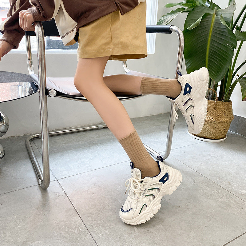 A woman wearing beige ribbed crew socks with white athletic sneakers, sitting in a modern chair against white background