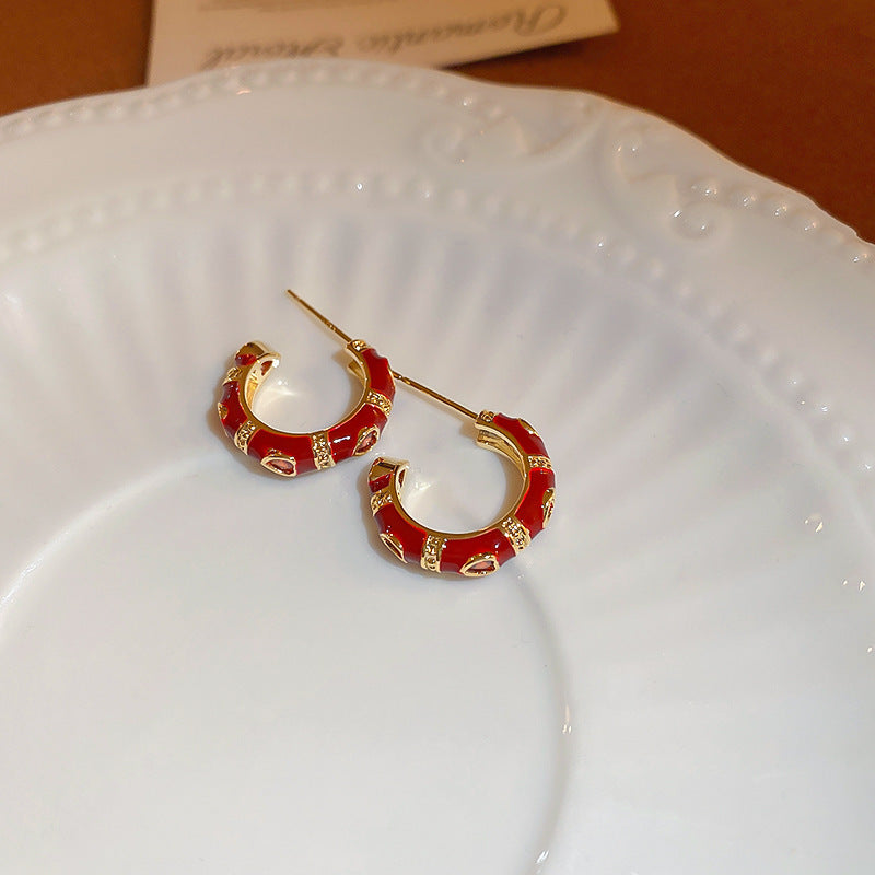 A pair of small red enamel hoop earrings with gold detailing is displayed on a white ceramic plate