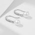 Elegant pearl drop earrings with silver hooks and crystal accents casting shadows on white surface