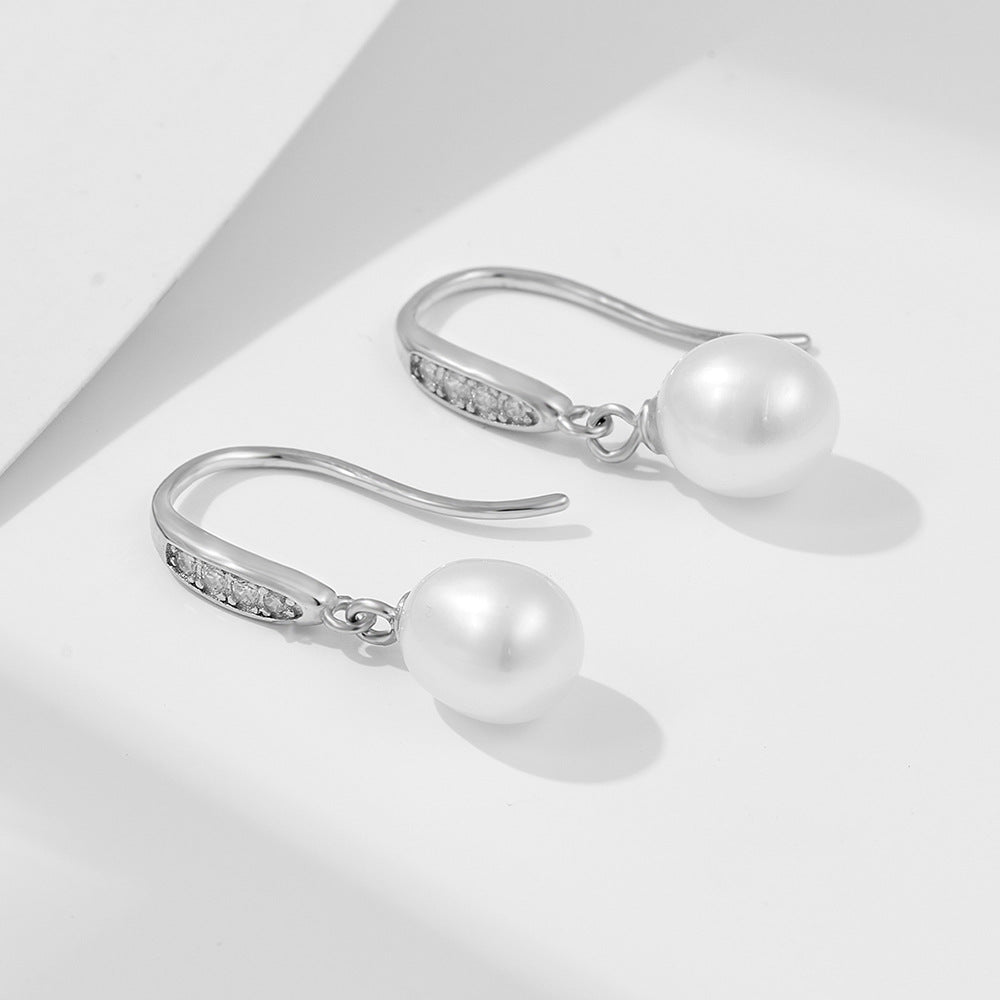 Elegant pearl drop earrings with silver hooks and crystal accents casting shadows on white surface