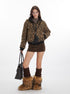 A woman wearing a leopard print bomber jacket with black trim paired with a brown corduroy mini skirt and furry boots, holding a black handbag against a white background