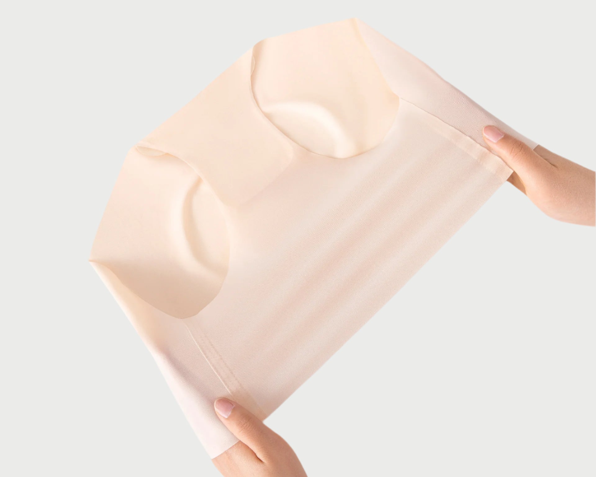 Hands demonstrating stretch of cream-colored seamless brief