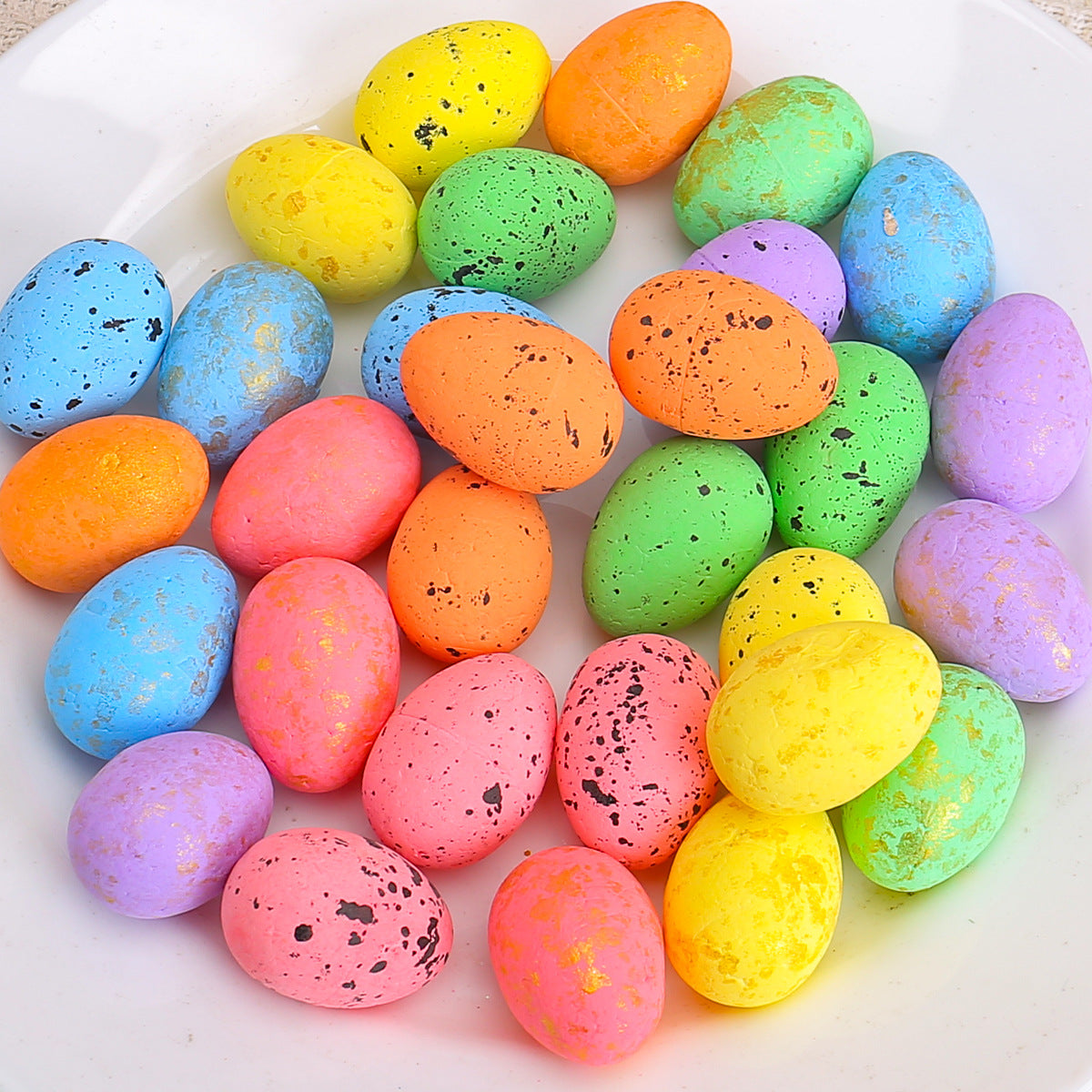 A close-up of multicolored speckled Easter eggs on a white plate, featuring vibrant pastel shades with gold and black speckles.