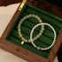 Two jade and pearl beaded bracelets displayed in a green-lined wooden jewelry box, featuring gold-toned details and small pendants