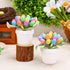 Two small white pots containing artificial Easter eggs in bright colors with green leaves, placed on a rustic wood slice against a spring-themed background.