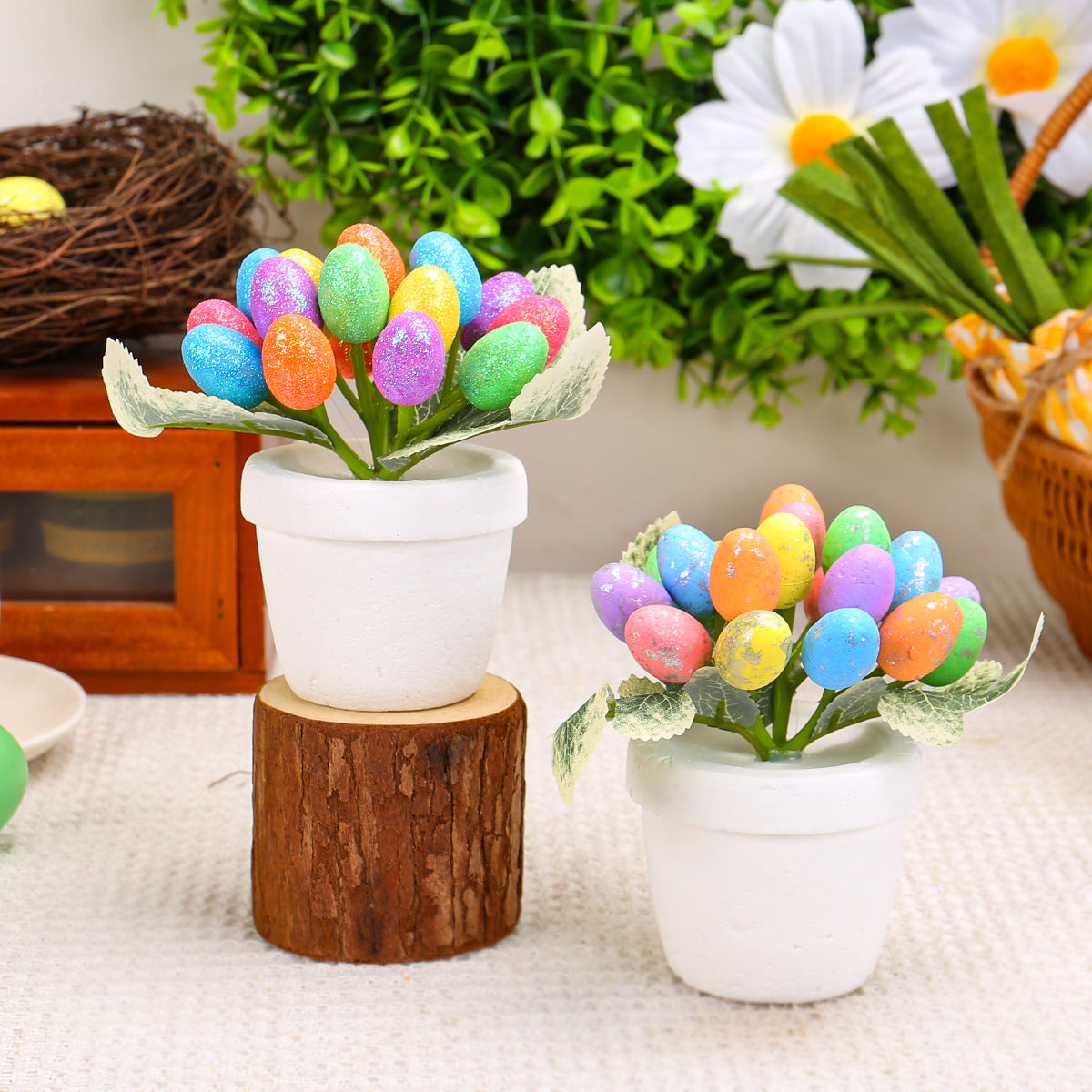 Two small white pots containing artificial Easter eggs in bright colors with green leaves, placed on a rustic wood slice against a spring-themed background.