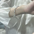 A silver curved bangle with bow charm worn on wrist against white bedding, photographed in soft natural light