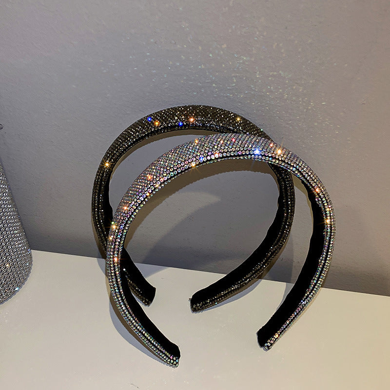 Two rhinestone-covered headbands, one black and one iridescent, displayed on a white surface with a subtle sparkle effect.
