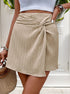 Front view of beige ribbed mini skirt with decorative twist detail at waist, shown with woven handbag and accessories
