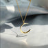 Gold crescent moon necklace with soft lighting creating dramatic shadows on light fabric