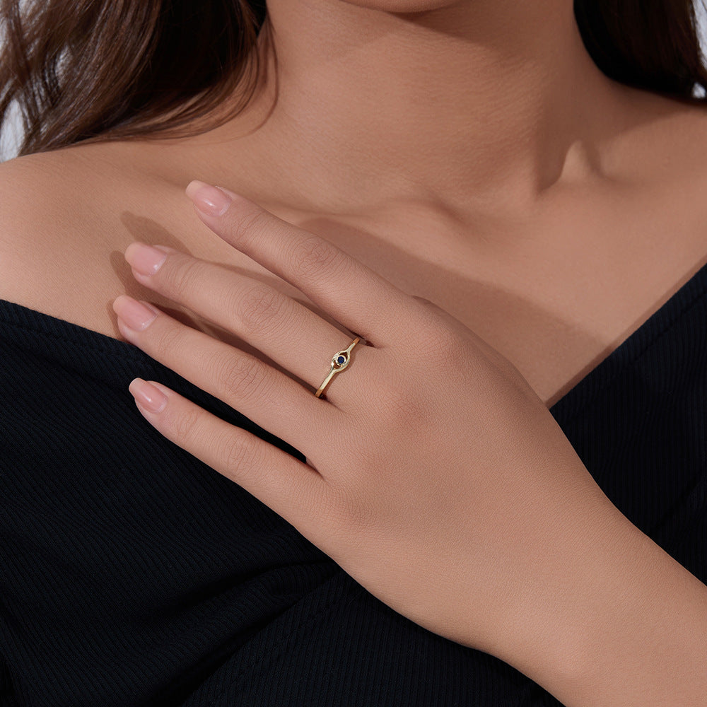 Close-up of a hand wearing delicate gold eye-shaped ring with blue sapphire against black clothing