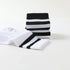 A close-up of folded black and white striped crew socks stacked on a white surface, showing ribbed texture and bold stripe details