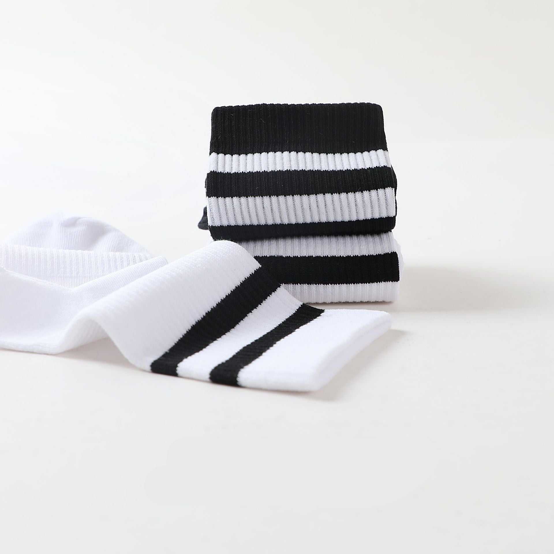 A close-up of folded black and white striped crew socks stacked on a white surface, showing ribbed texture and bold stripe details