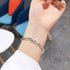 A model is wearing a silver twisted bangle bracelet on their wrist in a modern café setting with blue and orange chairs visible in the background