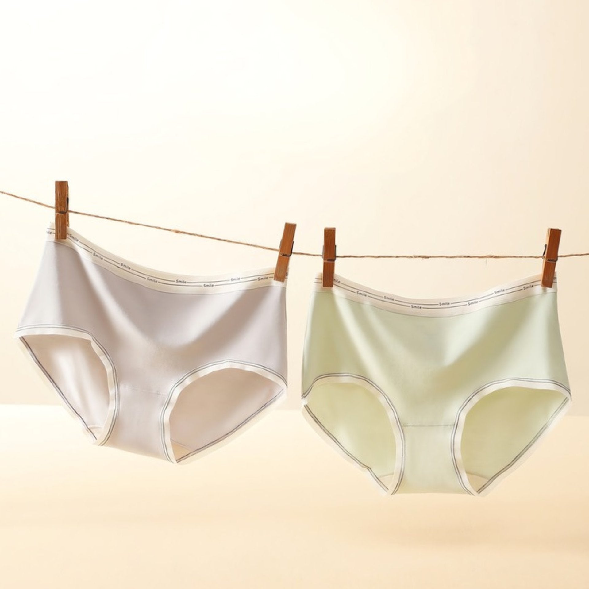 Two seamless briefs hanging on clothesline with wooden clips, shown in light nude and light green colors.