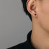 Small black round stud earring worn on ear, shown in profile against gray background
