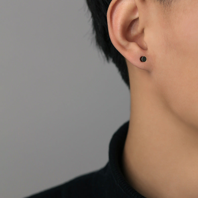 Small black round stud earring worn on ear, shown in profile against gray background