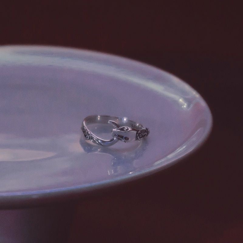 A silver snake-shaped ring with floral accents resting on a white ceramic plate against dark background