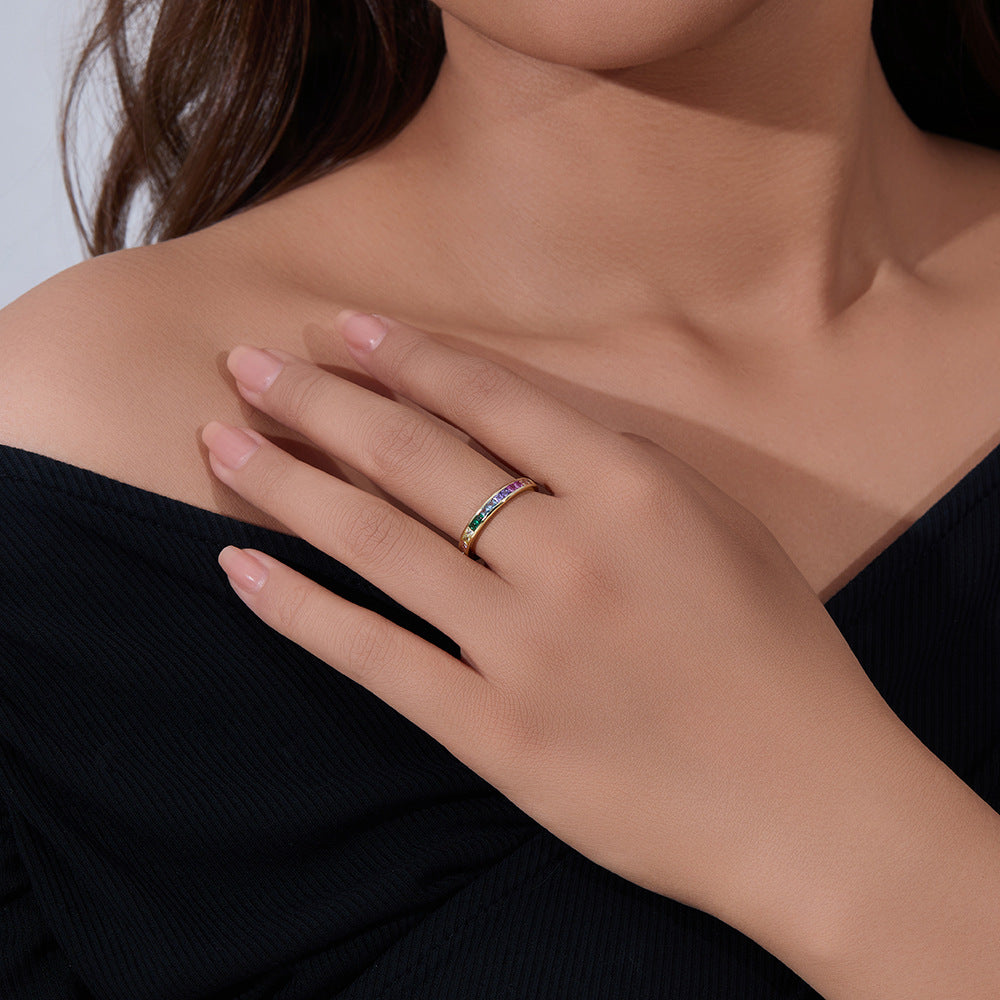 A gold rainbow eternity band with channel-set multicolored gemstones arranged in ROYGBIV order on white surface