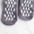 Close-up of gray non-slip socks with white footprint grip pattern on soles displayed against white fabric background