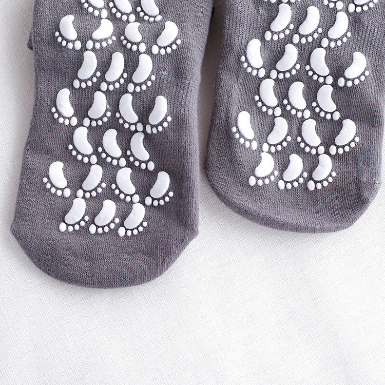 Close-up of gray non-slip socks with white footprint grip pattern on soles displayed against white fabric background